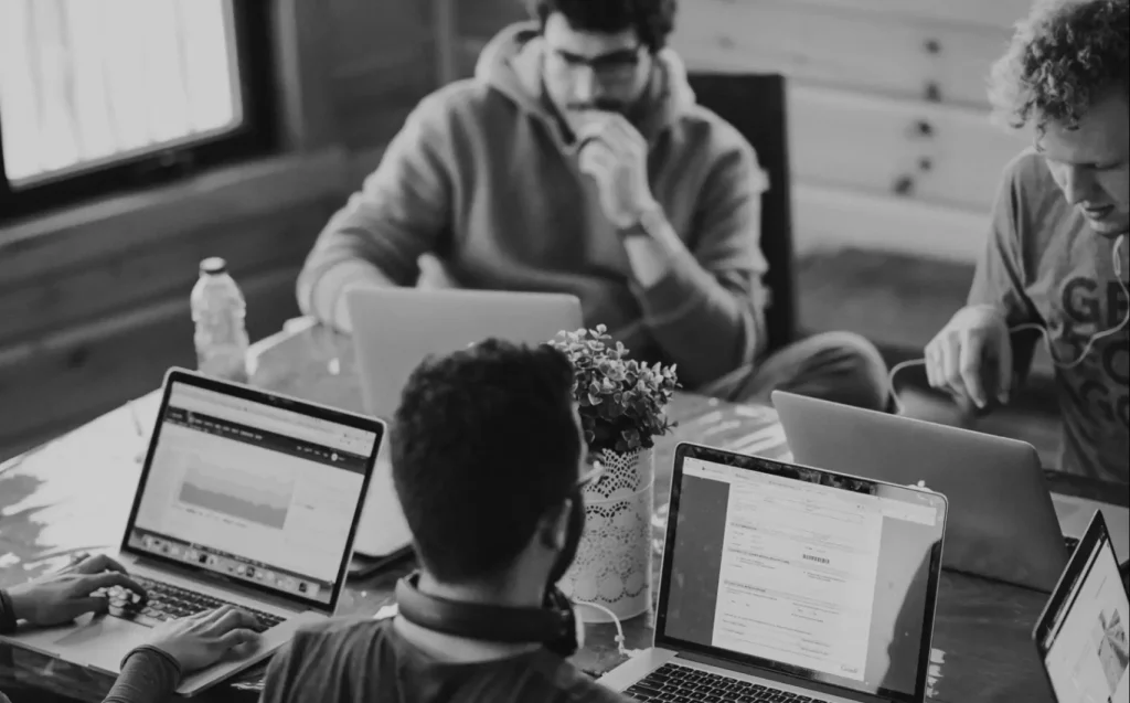 Eine Gruppe von Leuten, die gemeinsam an Laptops an einem Tisch arbeiten, in Schwarz-Weiß